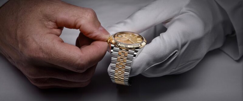 Hands holding a two-tone Rolex wristwatch during inspection