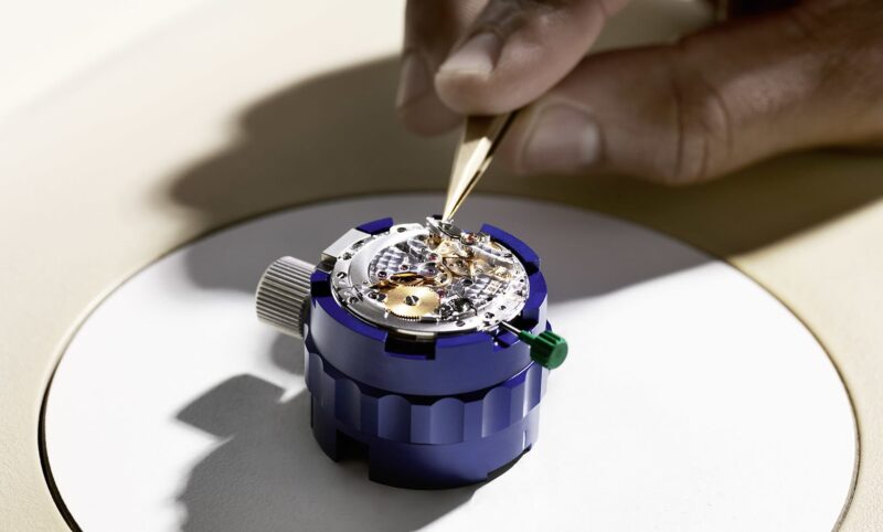 Watchmaker using a tool on a Rolex movement in a blue holder