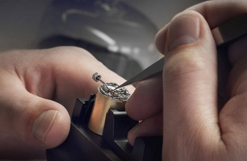 Watchmaker’s hands using tweezers on a movement in a holder