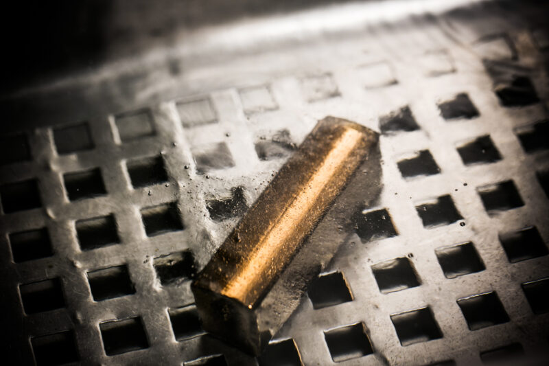 Gold-coloured metal bar on a perforated industrial surface in Chopard photography