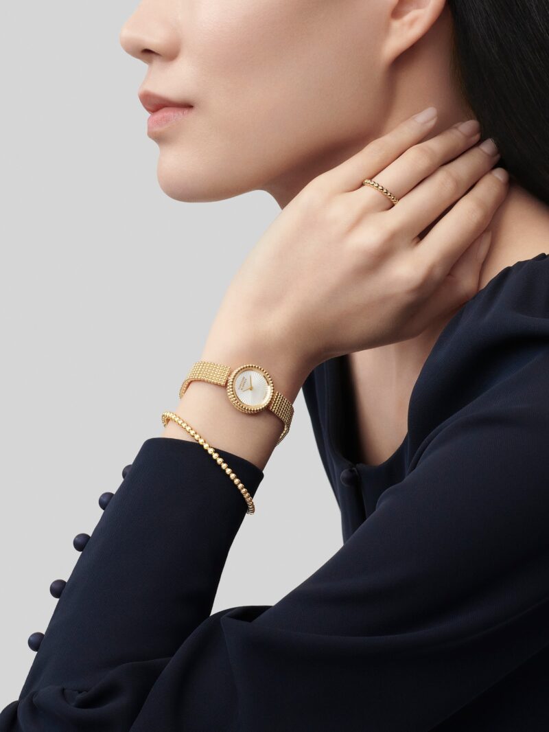 Round gold-tone Van Cleef & Arpels watch worn with a dark jacket