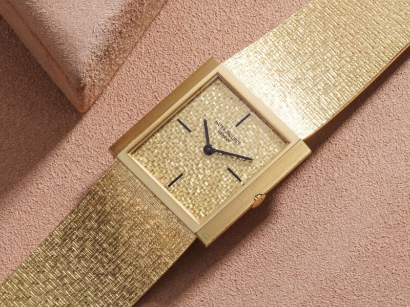 Rectangular gold-tone watch with a textured bracelet photographed on fabric by Phillips
