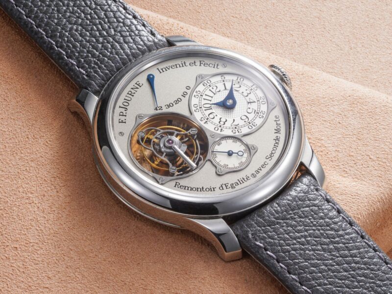 Round F.P. Journe watch with an exposed mechanism and grey strap photographed on textured fabric by Phillips