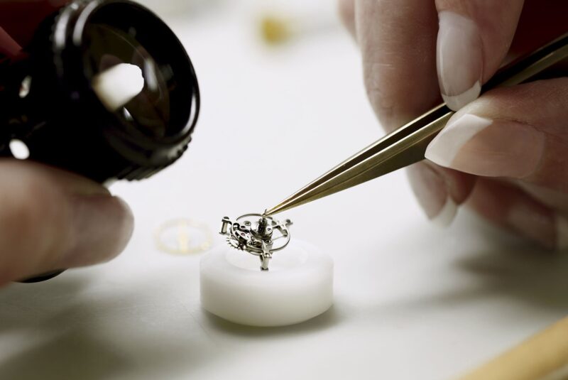 A watch component examined with tweezers and a loupe at Audemars Piguet