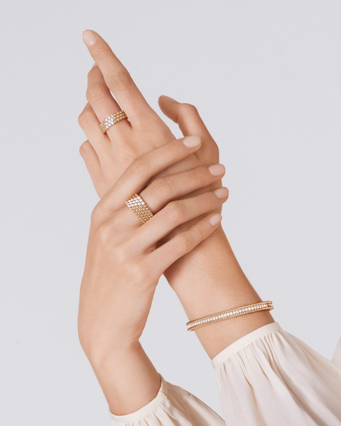 Close-up of a model hands wearing yellow gold Van Cleef & Arpels Perlee rings and a beaded Perlee bracelet
