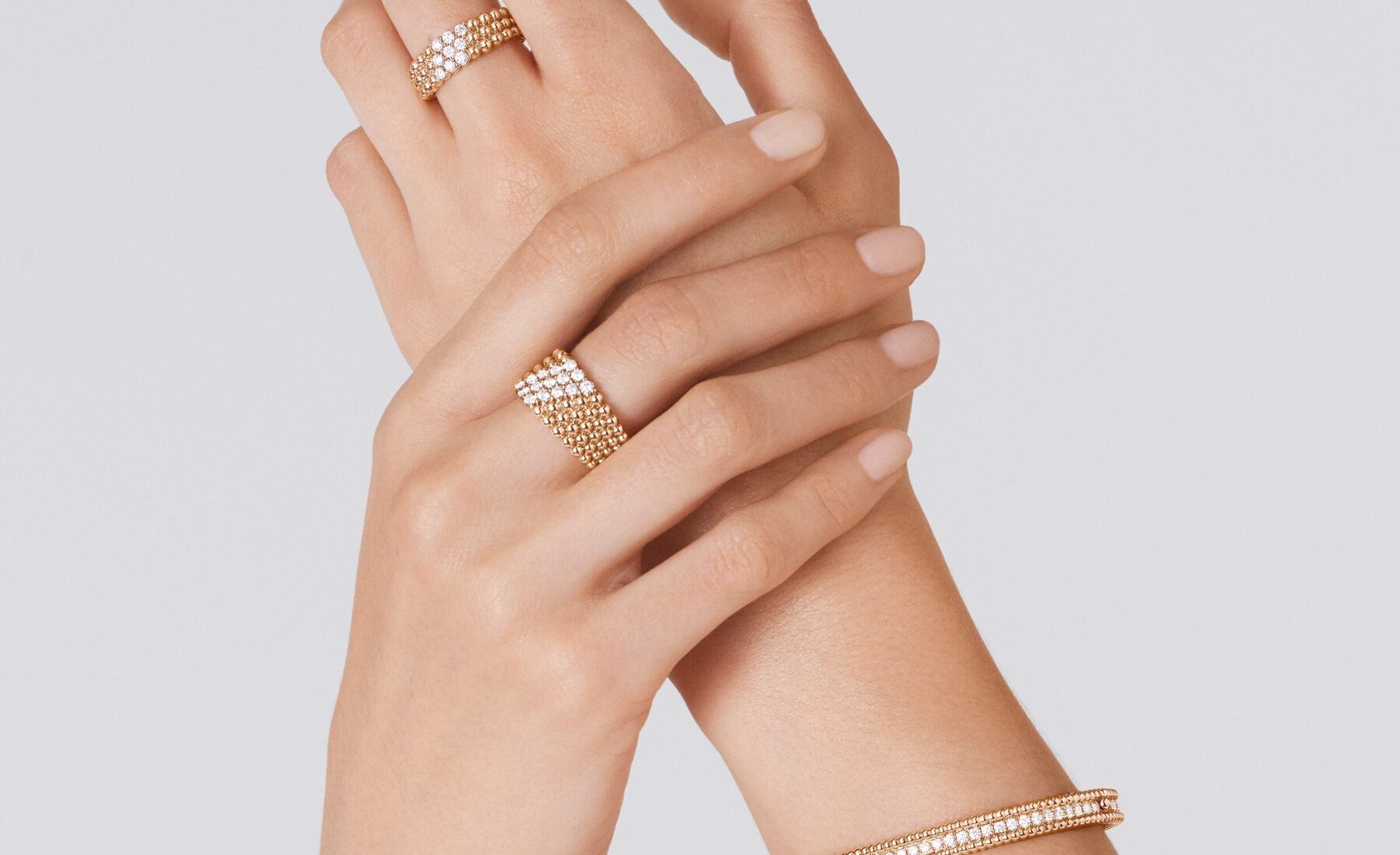 Close-up of a model hands wearing yellow gold Van Cleef & Arpels Perlee rings and a beaded Perlee bracelet