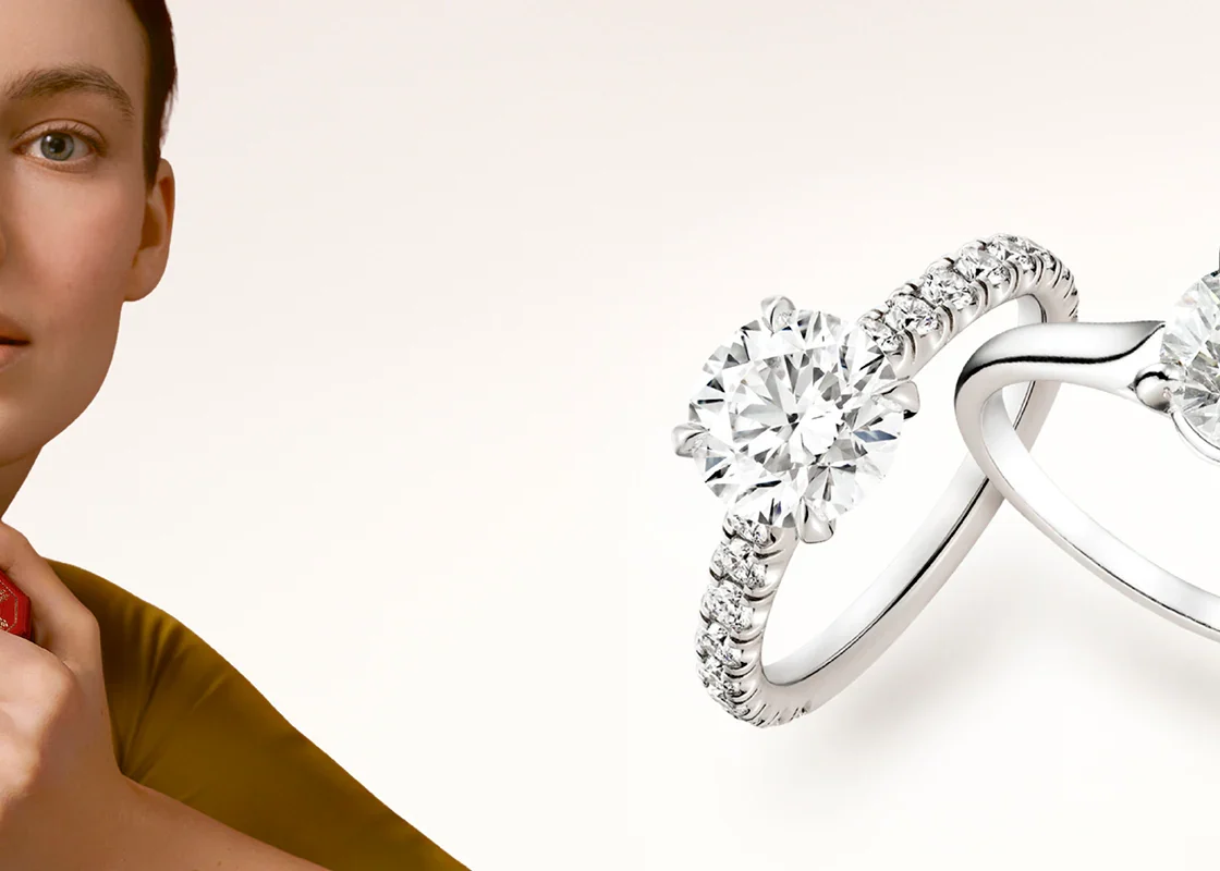 The Cartier Solitaire 1895 engagement ring resting on a white surface next to an open signature red Cartier ring box