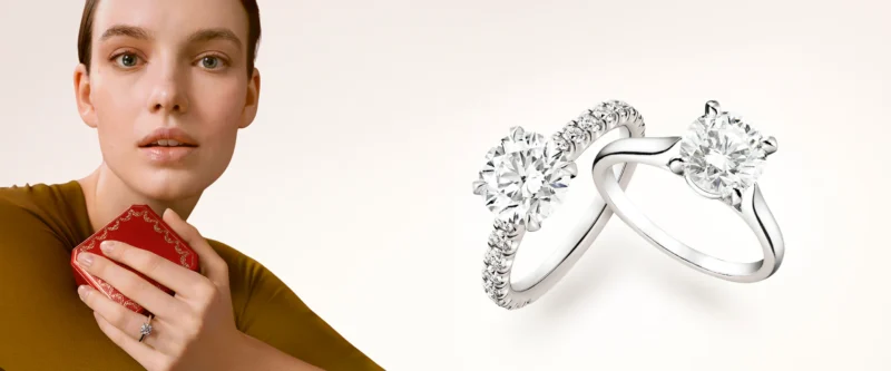 The Cartier Solitaire 1895 engagement ring resting on a white surface next to an open signature red Cartier ring box