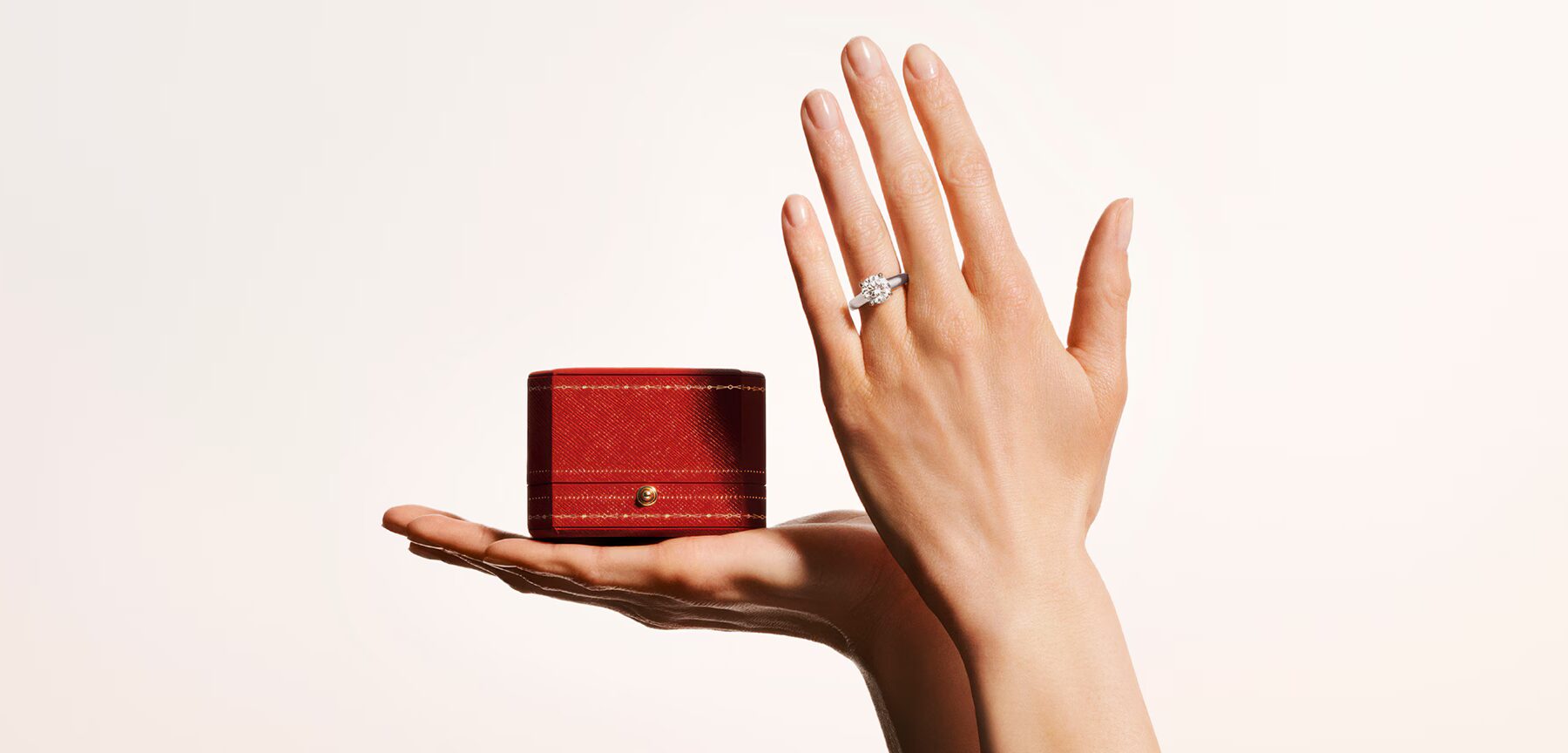 Wide lifestyle banner showing a model's hand wearing a Cartier Solitaire 1895 ring resting on a surface