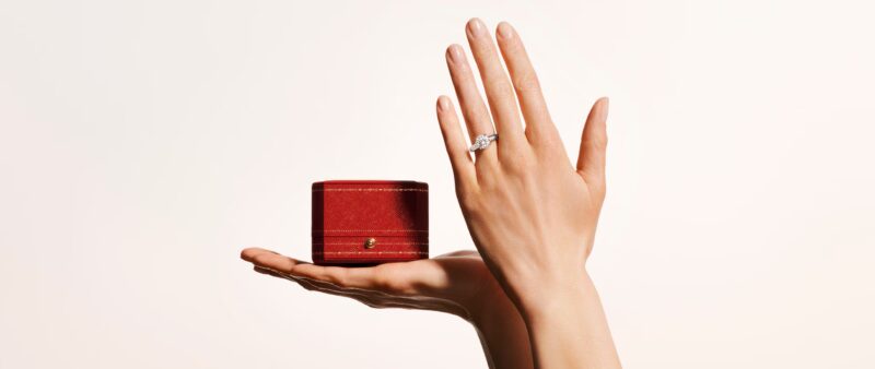 Wide lifestyle banner showing a model's hand wearing a Cartier Solitaire 1895 ring resting on a surface