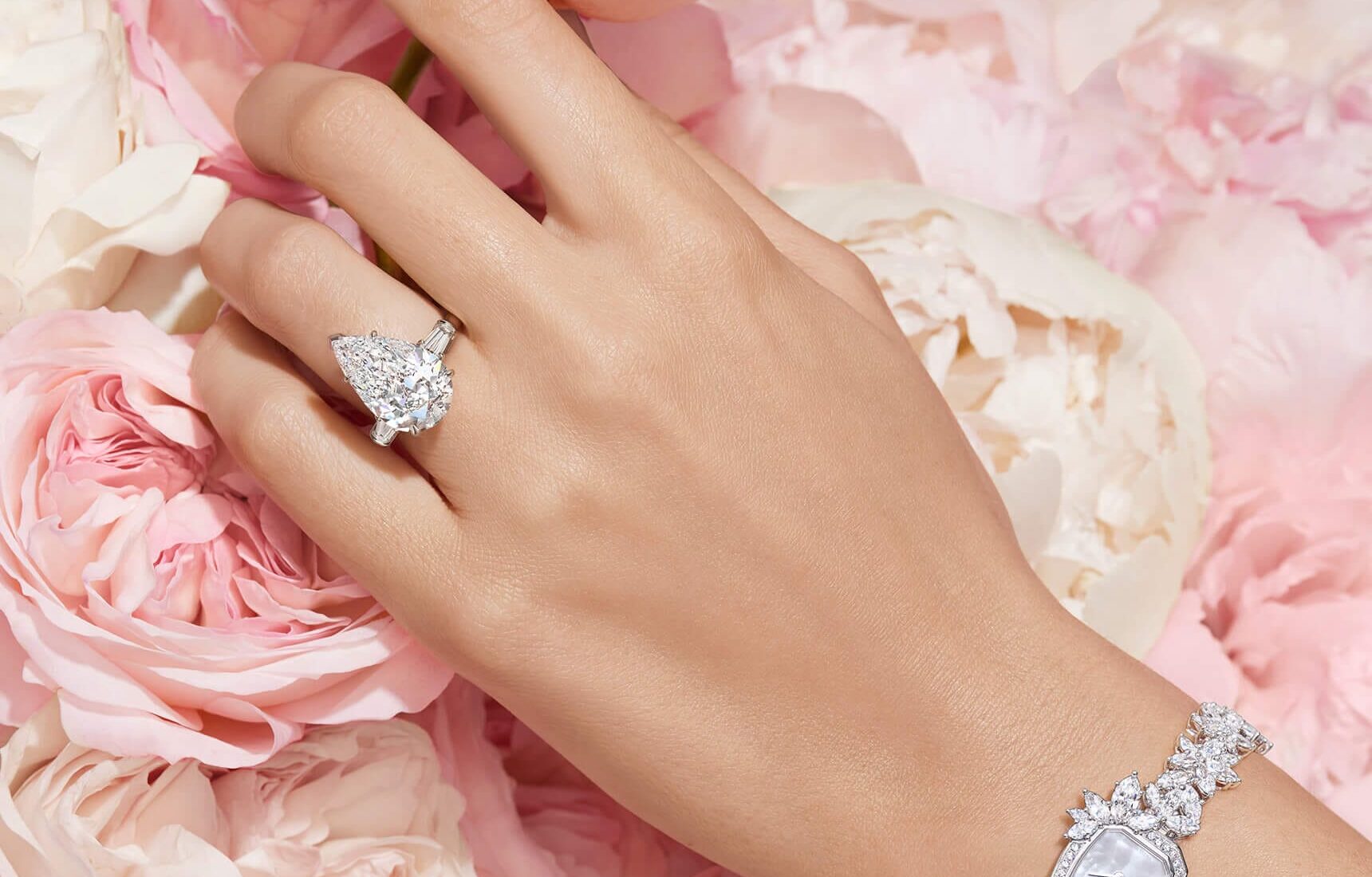 Close-up of a model hand wearing a Harry Winston pear-shaped solitaire engagement ring against a soft background
