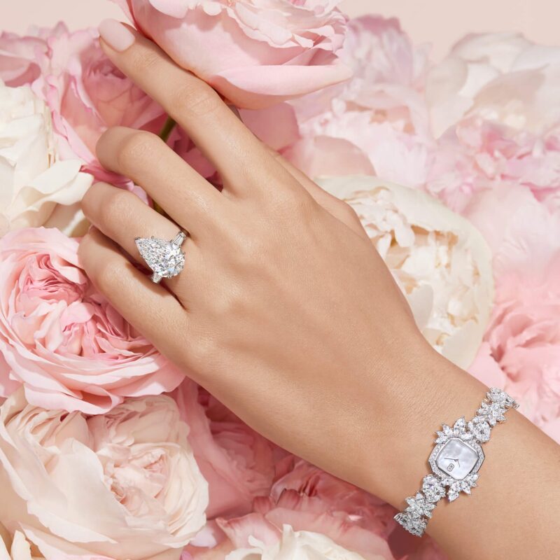 Close-up of a model hand wearing a Harry Winston pear-shaped solitaire engagement ring against a soft background