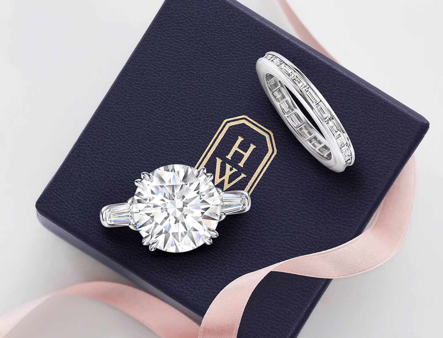 A Harry Winston Classic round brilliant solitaire diamond engagement ring and matching diamond wedding band resting in a navy blue velvet presentation box