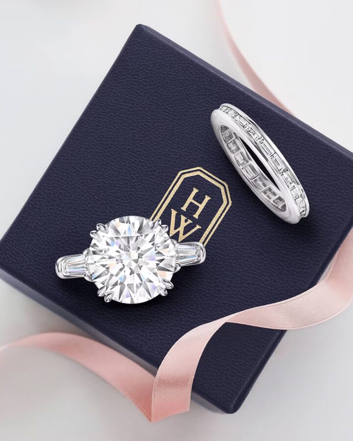 A Harry Winston Classic round brilliant solitaire diamond engagement ring and matching diamond wedding band resting in a navy blue velvet presentation box