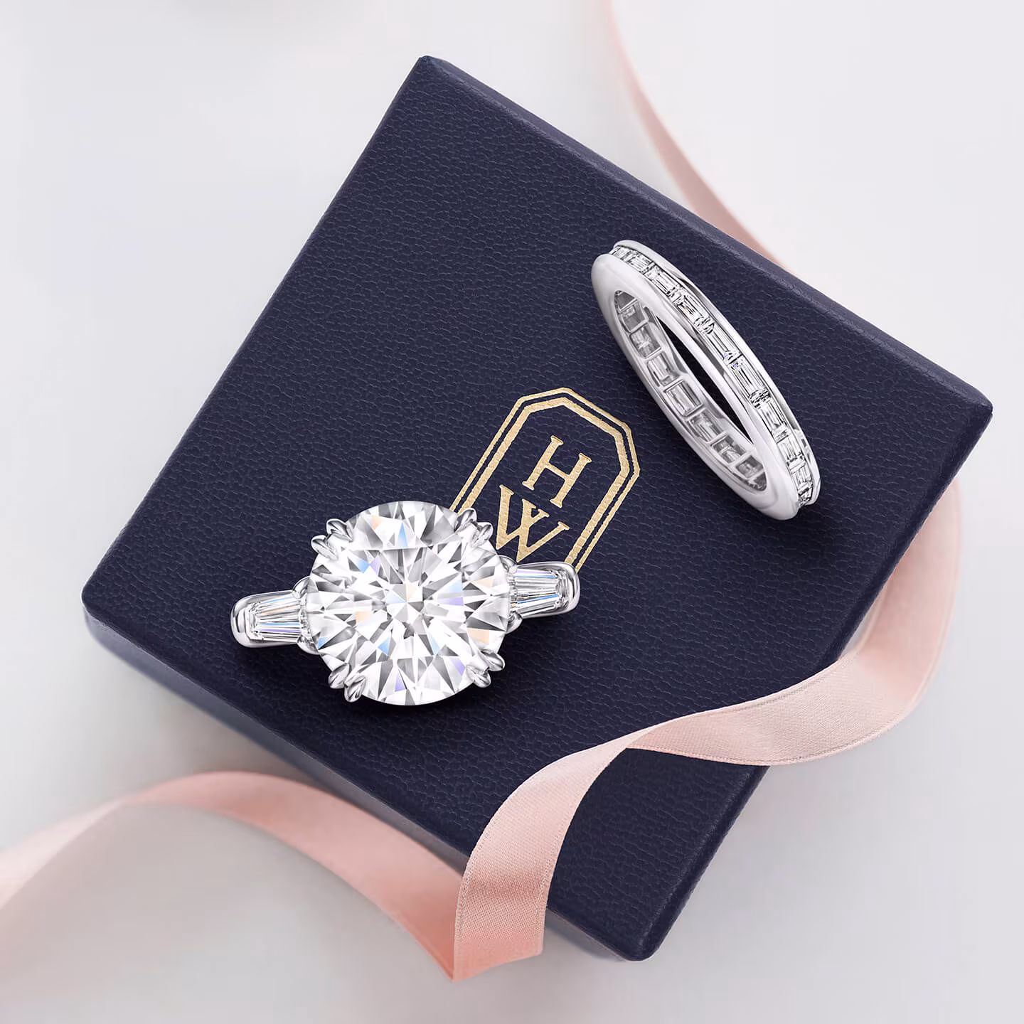 A Harry Winston Classic round brilliant solitaire diamond engagement ring and matching diamond wedding band resting in a navy blue velvet presentation box