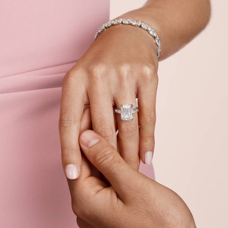 Model wearing an emerald-cut Harry Winston solitaire engagement ring and a micropave band on her finger