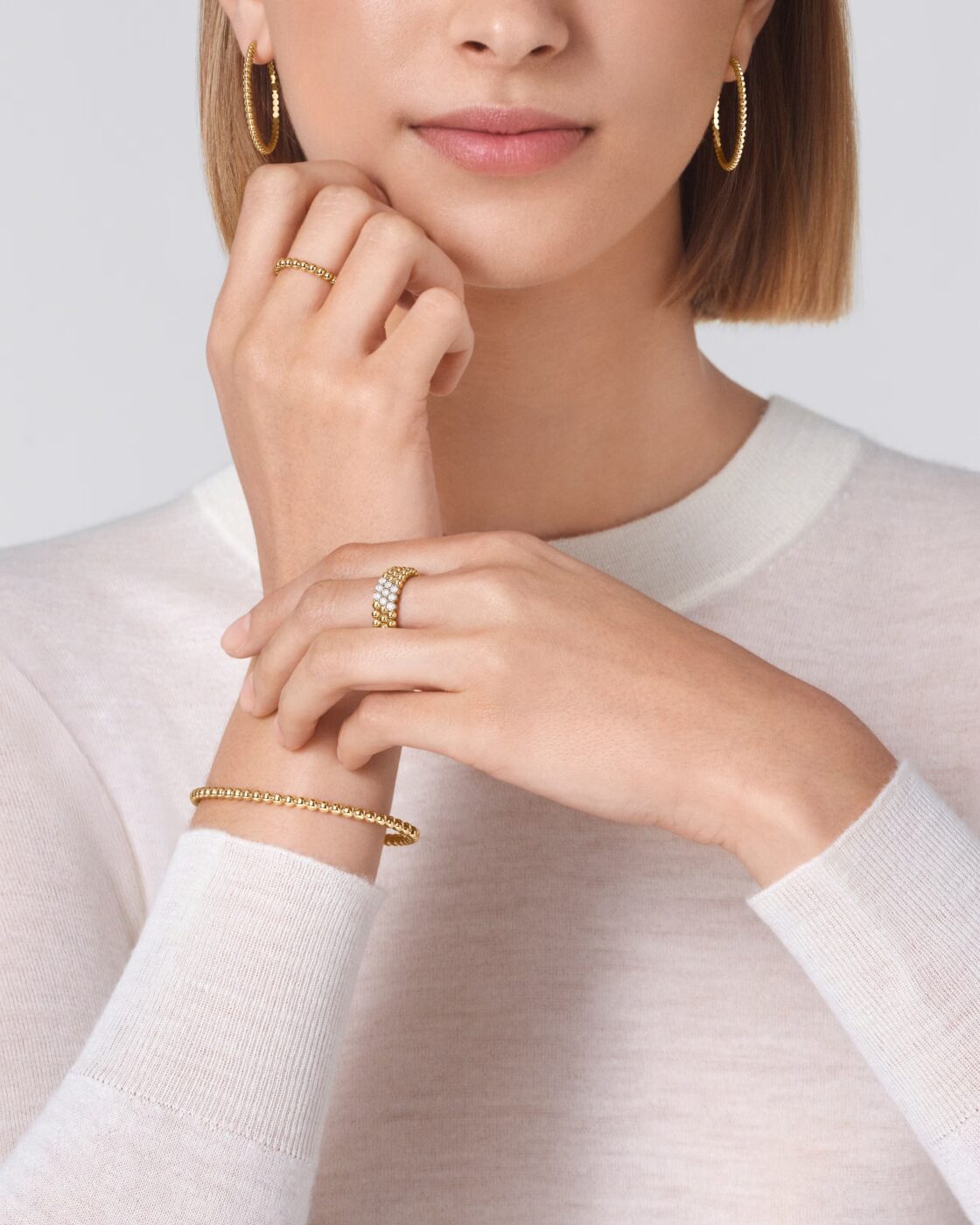 Close-up of a model wearing yellow gold Van Cleef & Arpels Perlee beaded hoop earrings, a ring, and a bracelet