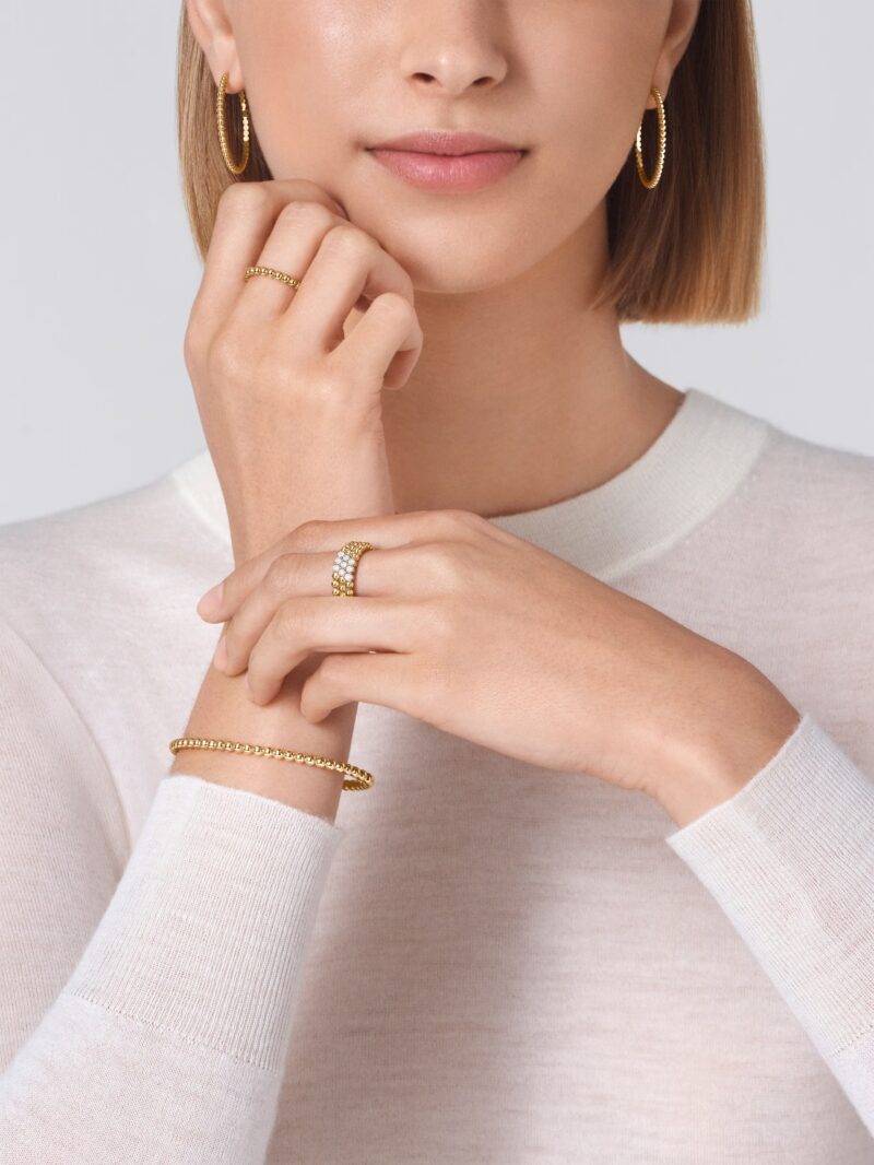 Close-up of a model wearing yellow gold Van Cleef & Arpels Perlee beaded hoop earrings, a ring, and a bracelet
