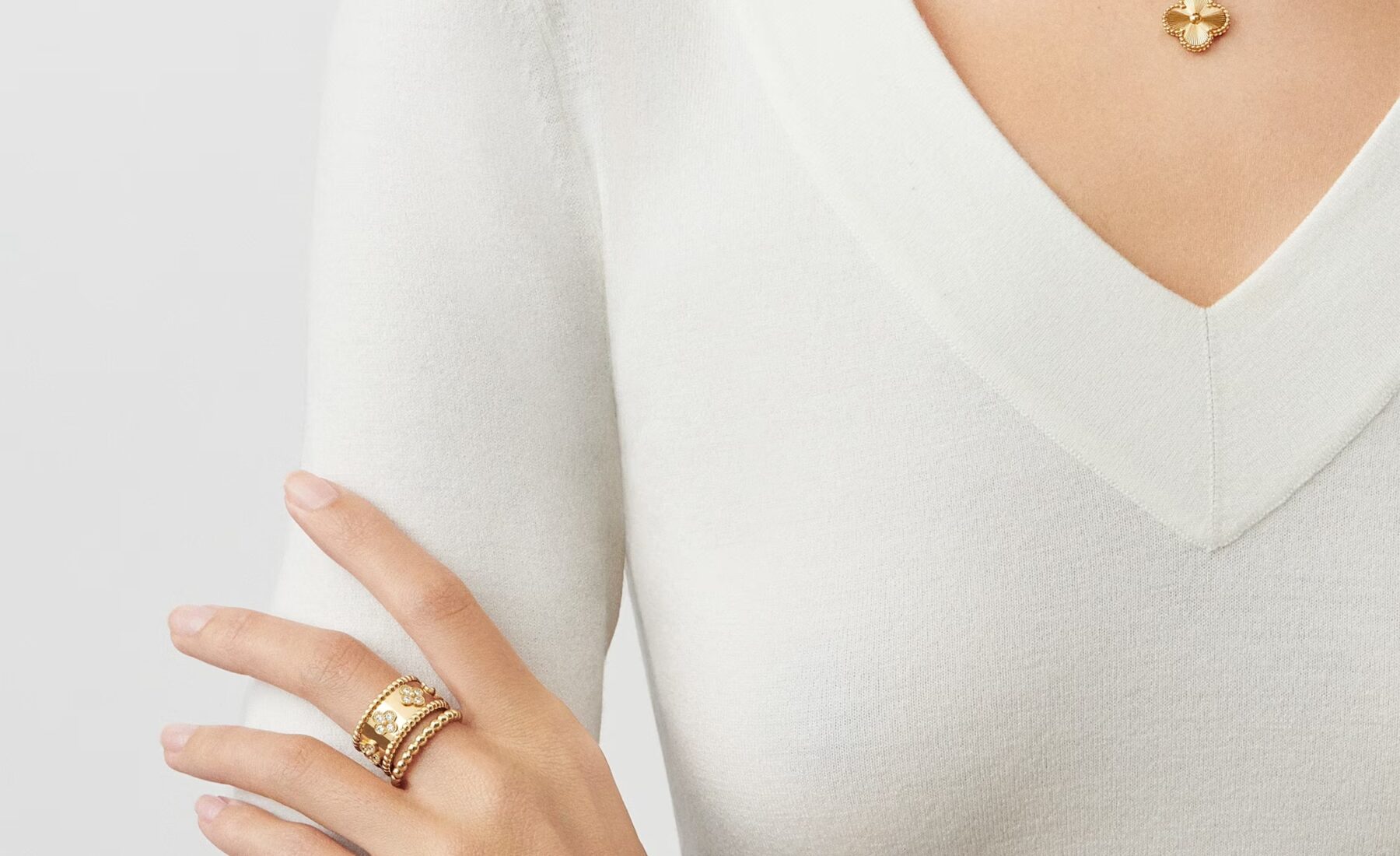 Woman in white V-neck top wearing a wide yellow gold Perlée diamond-paved ring, a Sweet Alhambra mother-of-pearl bracelet, and a matching Sweet Alhambra pendant