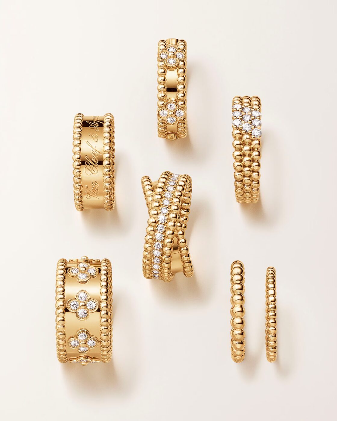 Flat-lay photo of six Perlée rings in yellow gold, including signature engraved ring, diamond clover ring, crossover ring, and simple beaded bands
