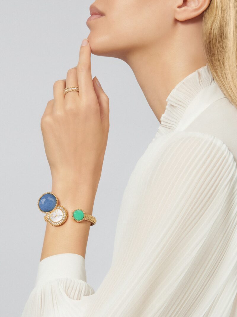 Blonde model in profile wearing a white high-neck top, Perlée ring, and Perlée Toi & Moi secret watch on her wrist