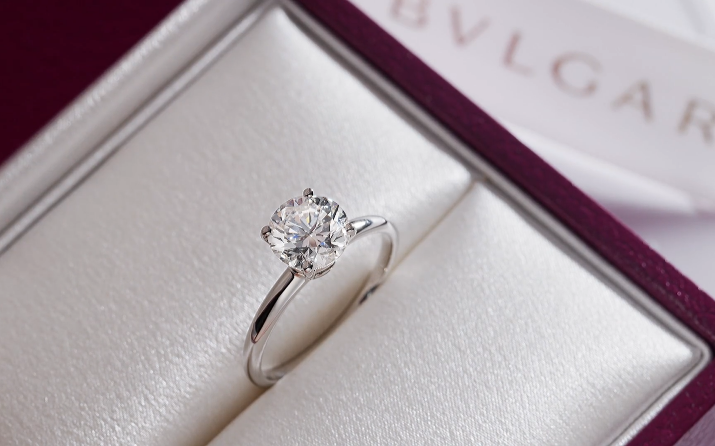 A Bulgari solitaire engagement ring inside its custom open burgundy presentation box with soft lighting