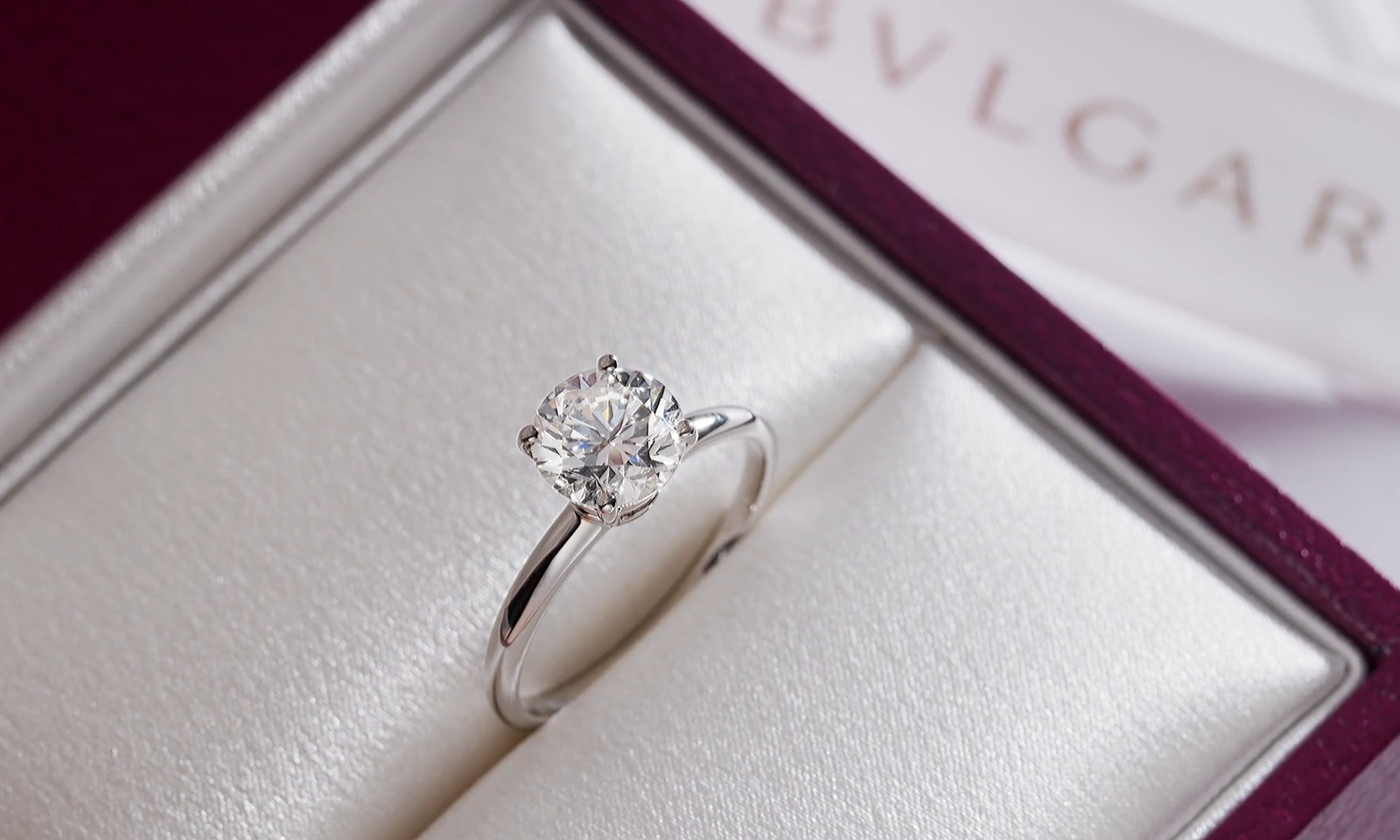 A Bulgari solitaire engagement ring inside its custom open burgundy presentation box with soft lighting