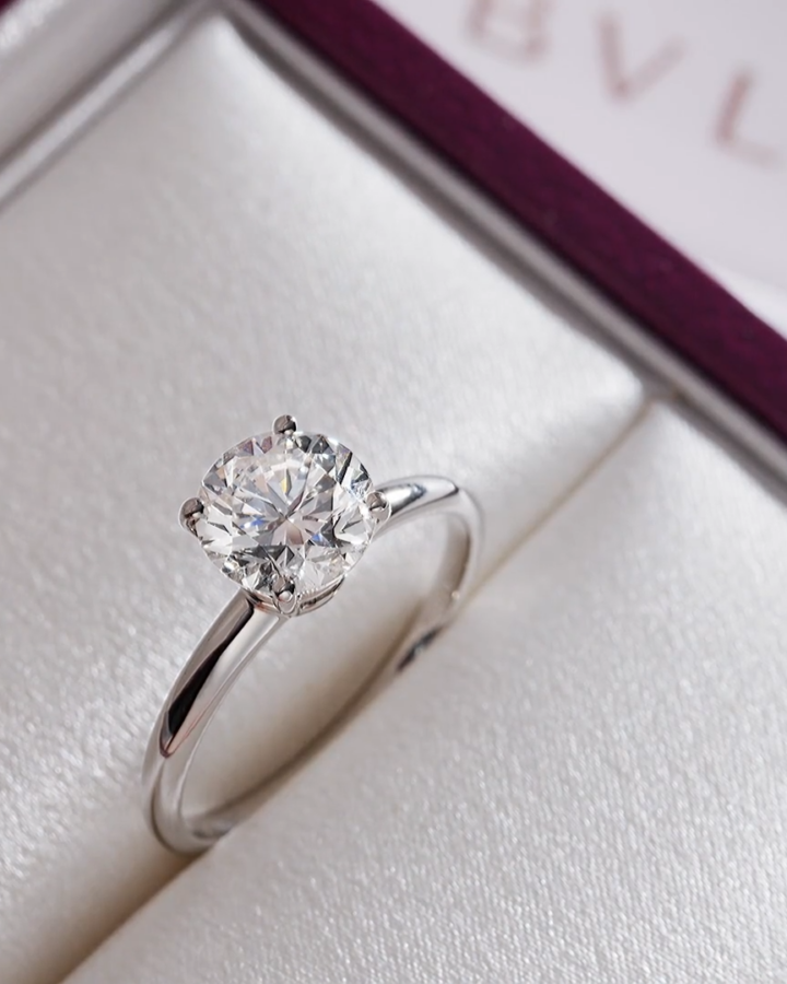 A Bulgari solitaire engagement ring inside its custom open burgundy presentation box with soft lighting