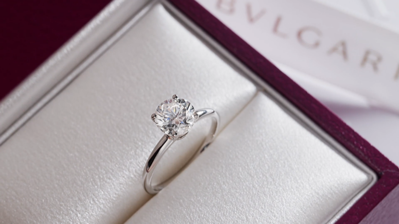 A Bulgari solitaire engagement ring inside its custom open burgundy presentation box with soft lighting