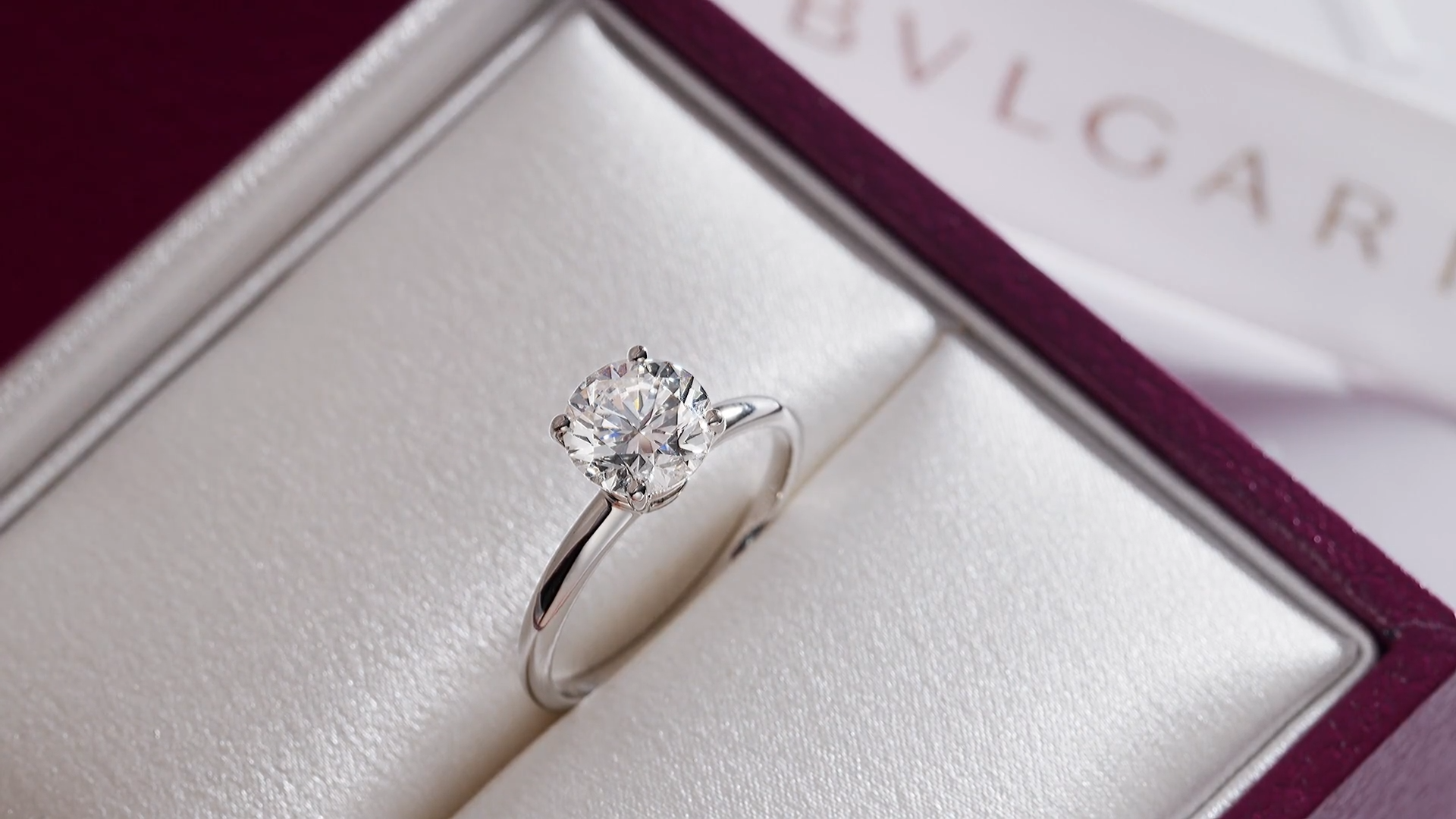 A Bulgari solitaire engagement ring inside its custom open burgundy presentation box with soft lighting