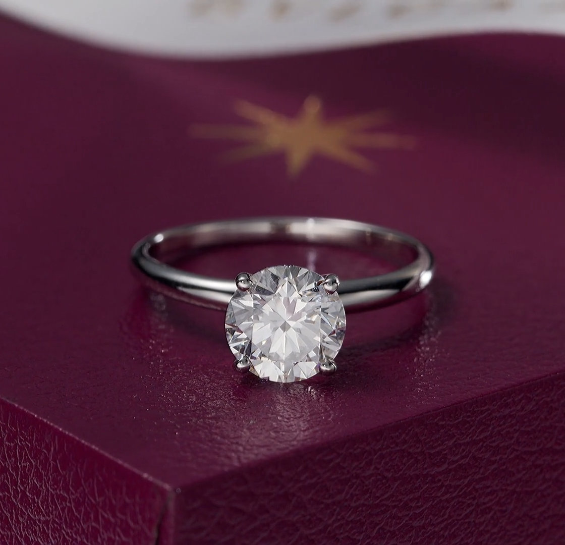 A Bulgari solitaire engagement ring sitting on top of its closed burgundy presentation box