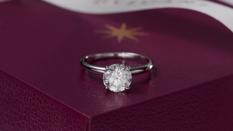 A Bulgari solitaire engagement ring sitting on top of its closed burgundy presentation box