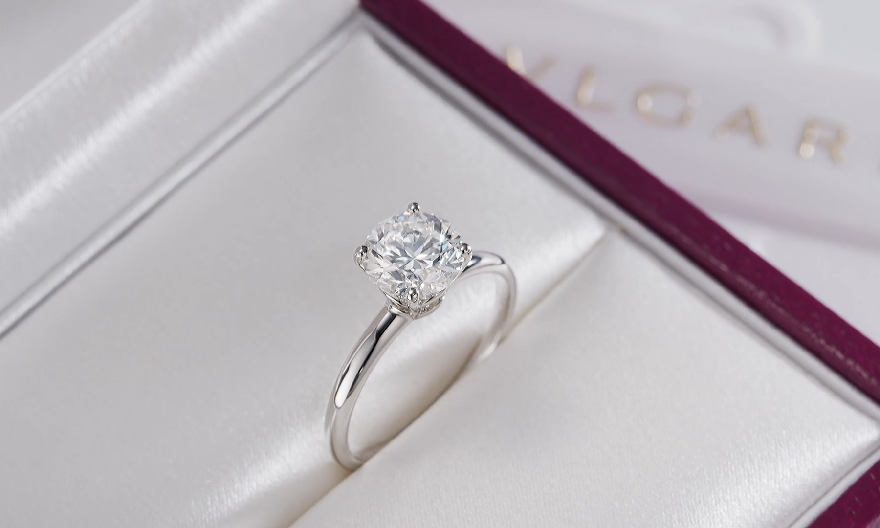 Burgundy Bulgari presentation box open showing an engagement ring against a soft background