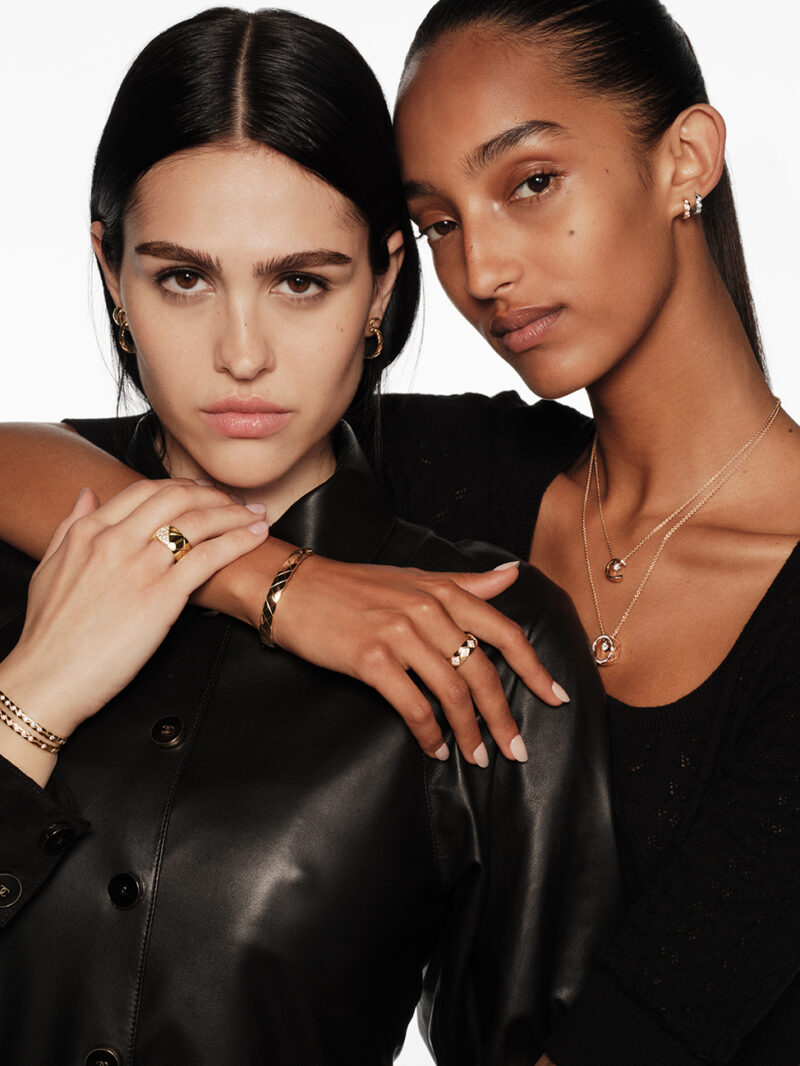 Two models wearing CHANEL COCO CRUSH rings, bracelets, necklaces and earrings in gold tones.