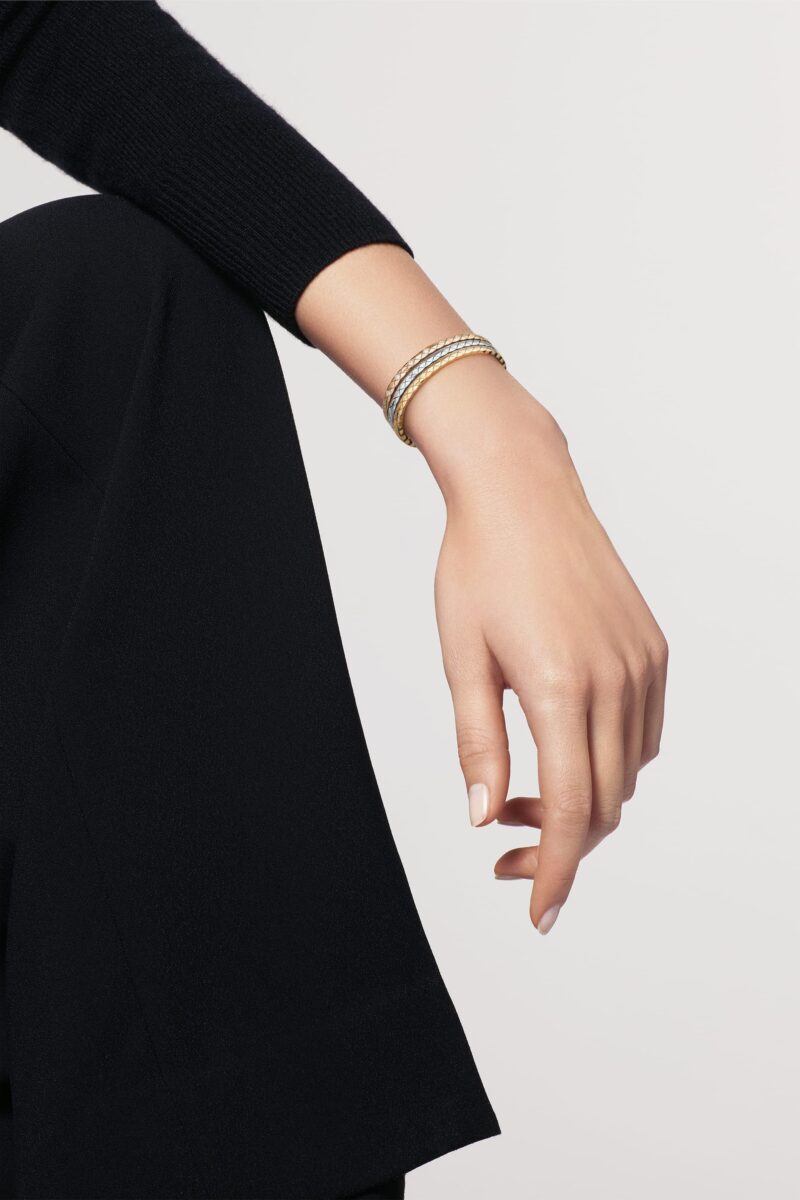 A hand against a black dress with several slim CHANEL COCO CRUSH bracelets stacked at the wrist.
