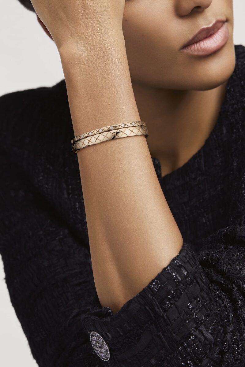 Model's wrist wearing two stacked CHANEL COCO CRUSH bracelets against black clothing.