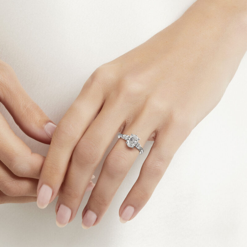Hand wearing a Graff Promise oval diamond ring with pear-shape side stones.