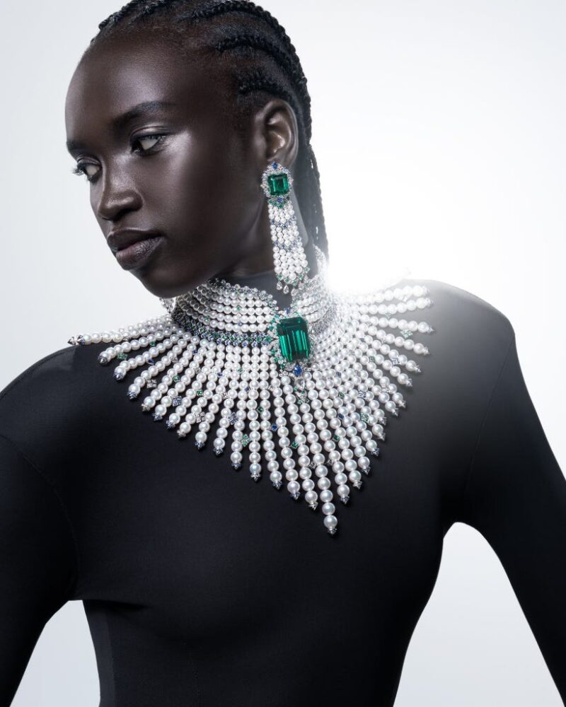 Model wearing Mikimoto L’éclat Solaire necklace and earrings with a pearl collar, large green centre and fanned descending strands.