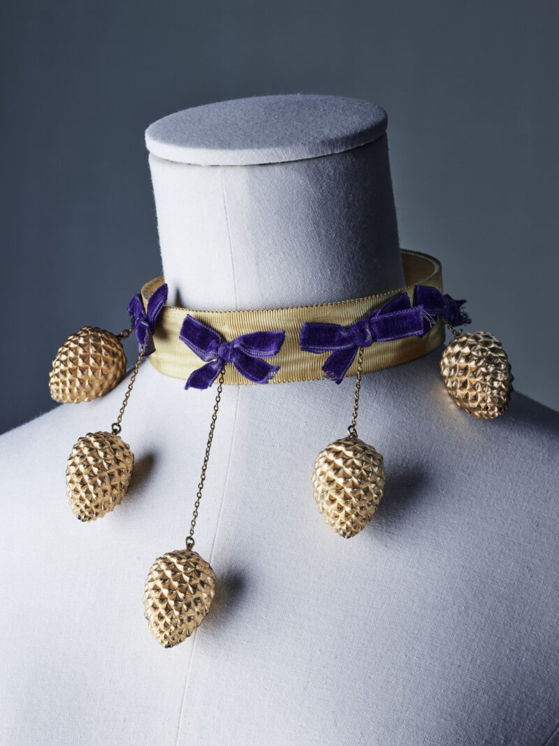 Pale choker with purple velvet bows and gilt pine cones suspended at different lengths.
