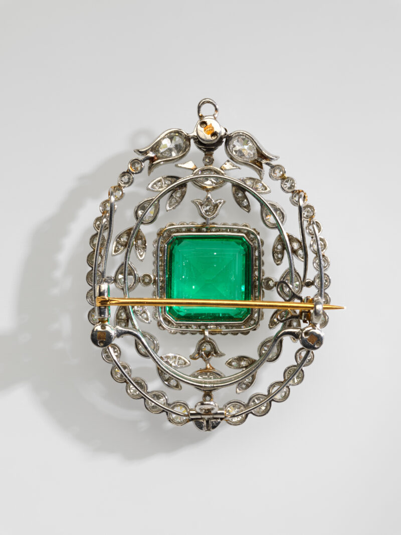 Angled reverse view of an emerald and diamond brooch, showing its pin and open setting.