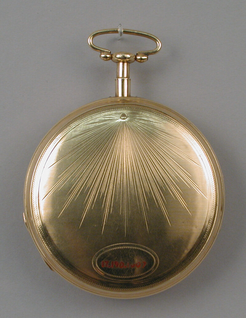 Closed gold back of a skeleton watch, with radiating engraved lines.