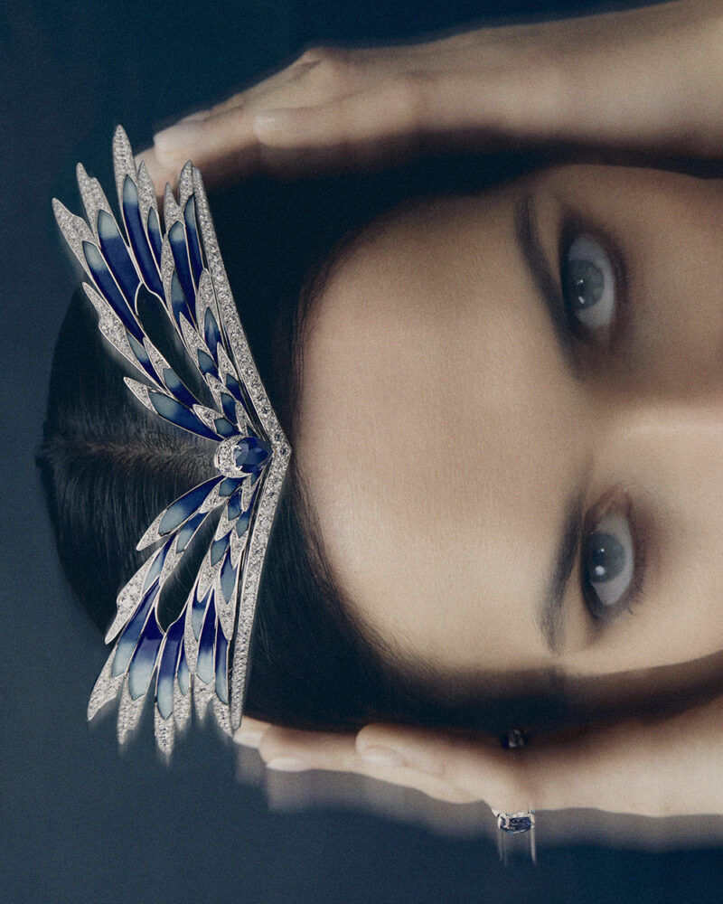 Sideways campaign portrait of a woman holding blue enamel and diamond wings across her forehead.