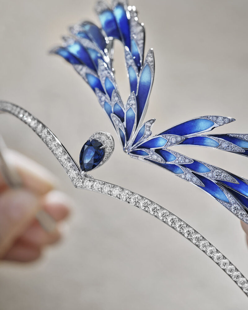 Close view of blue feather-shaped sections and bright stone-set lines on a tiara held in the workshop.