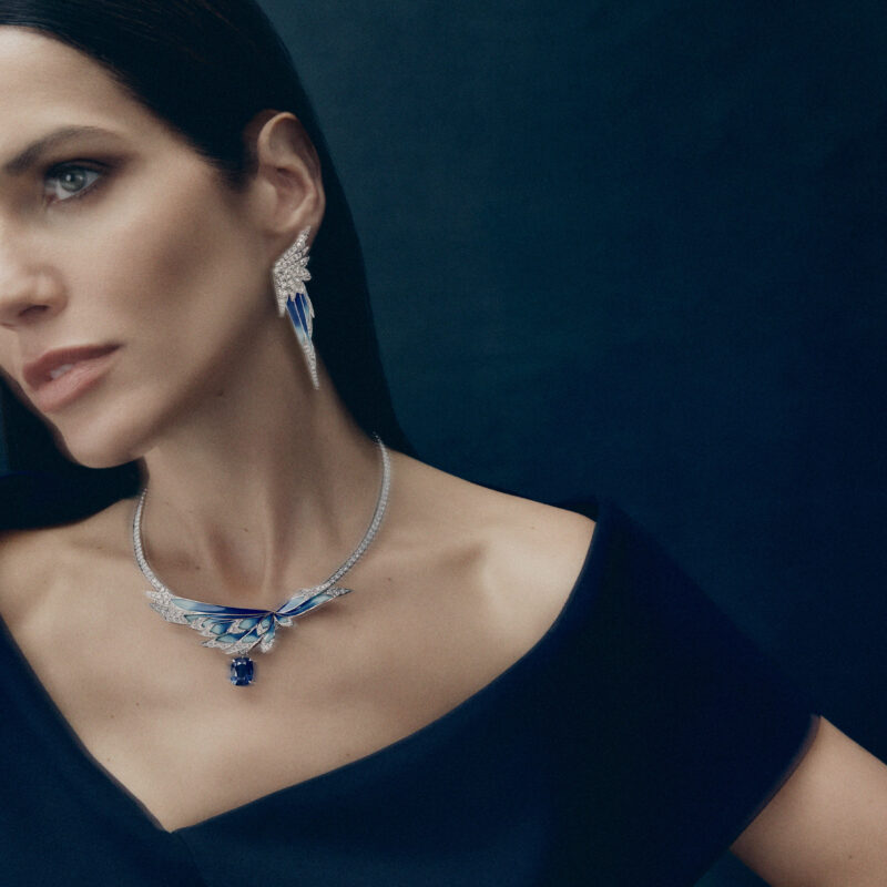 Woman in a dark dress wearing a blue winged necklace and a matching elongated earring.