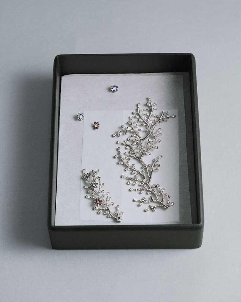 Dark-edged tray holding a branching floral jewel and smaller components on a pale surface.