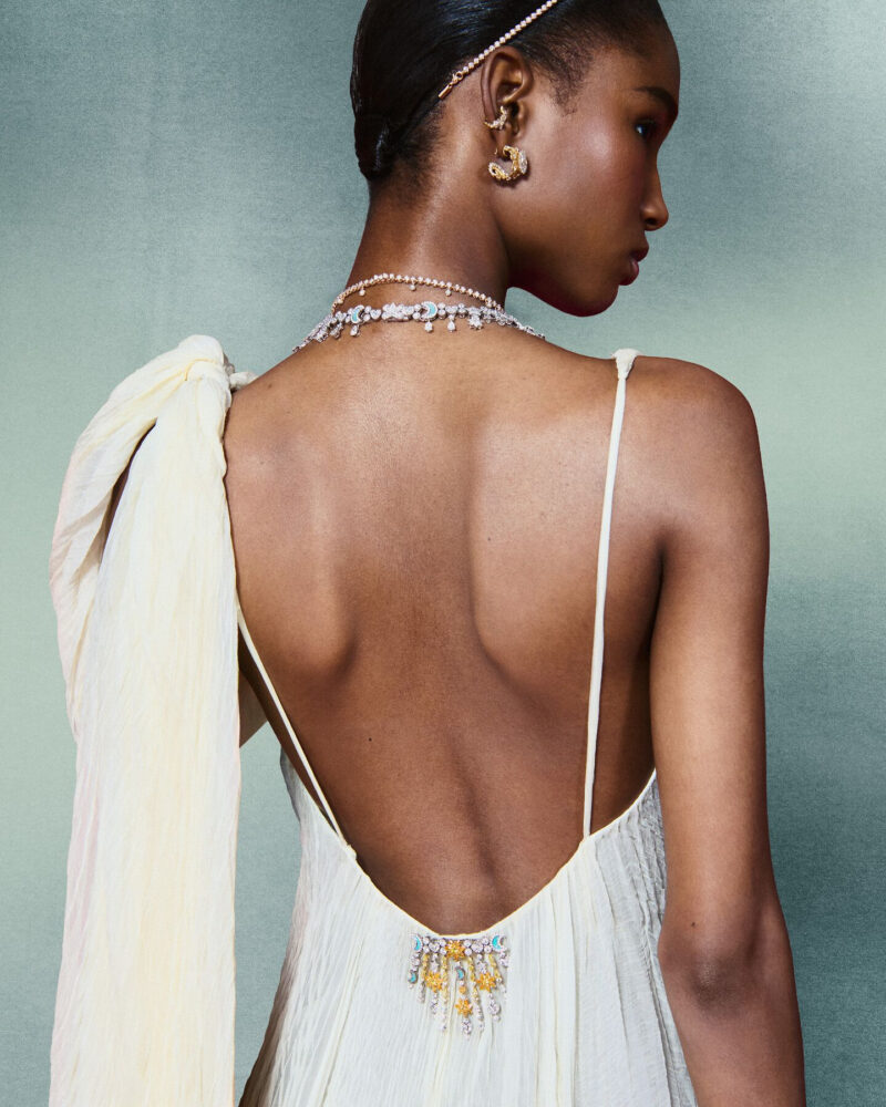 Woman seen from behind in an open-backed white dress with jewels at the neck and lower back.
