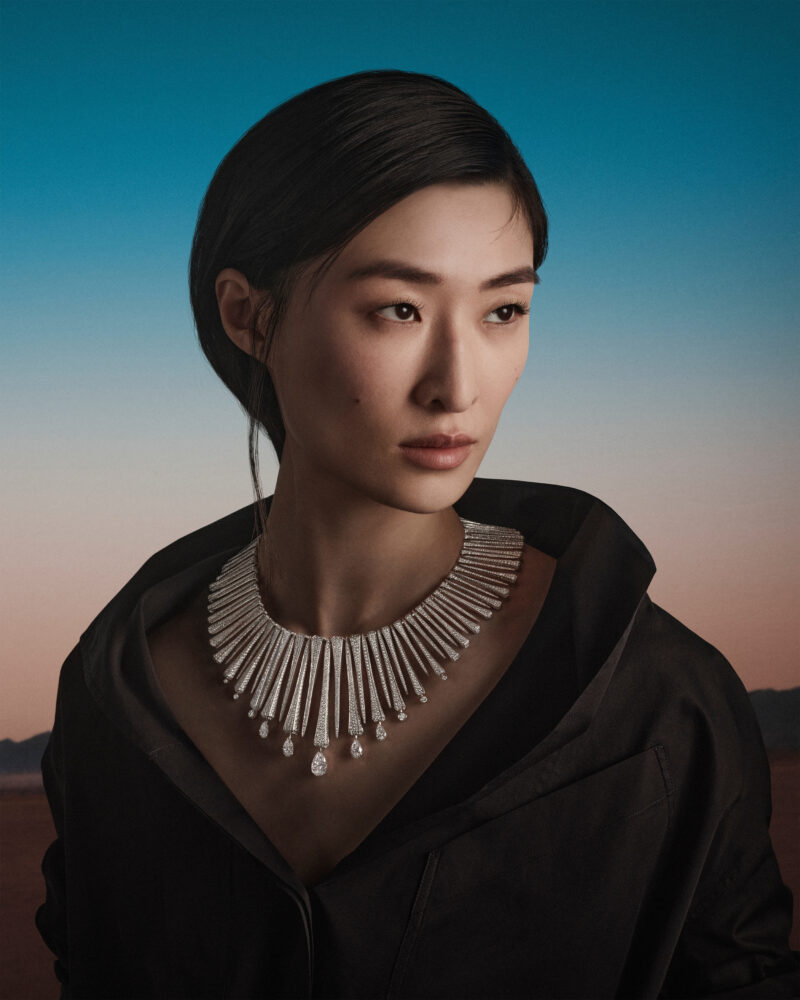 Woman in a black coat wearing a necklace of repeated bright elongated elements above the neckline.