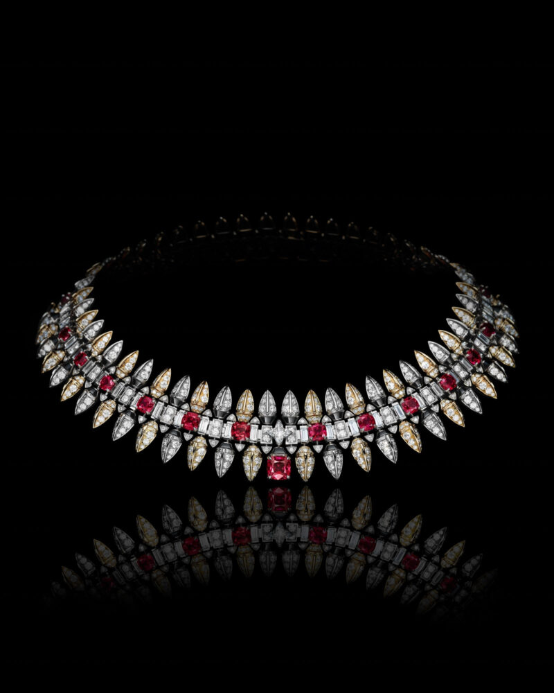 Conquest necklace against black with repeated red stones, dark borders and pointed bright elements.