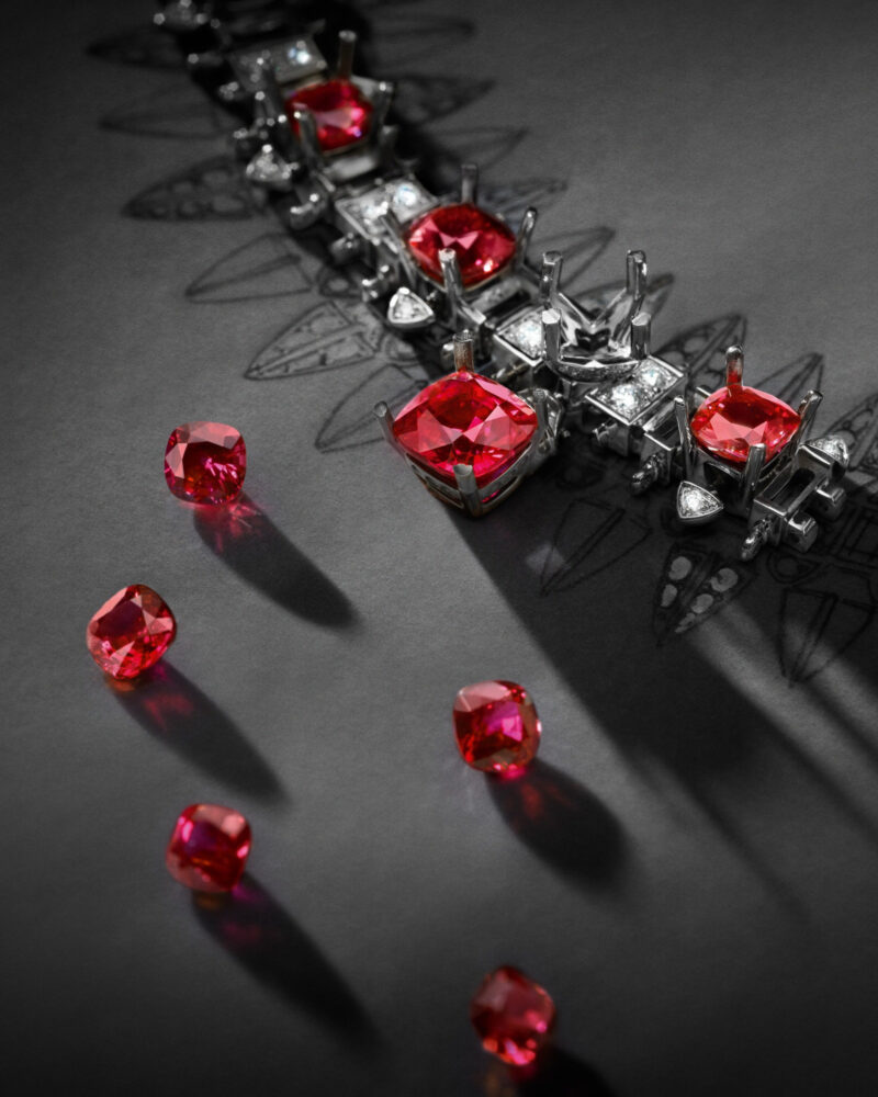 Loose red rubies beside the Conquest mounting during setting on a dark work surface.
