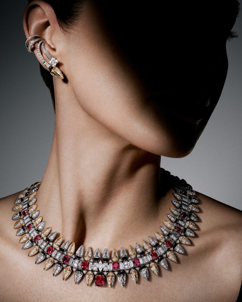 Woman turning her head away, the red and bright pointed Conquest necklace following the side of her neck.
